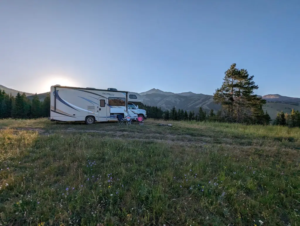 A Class C camper parked in a meadow with mountains in the backdrop during sunset